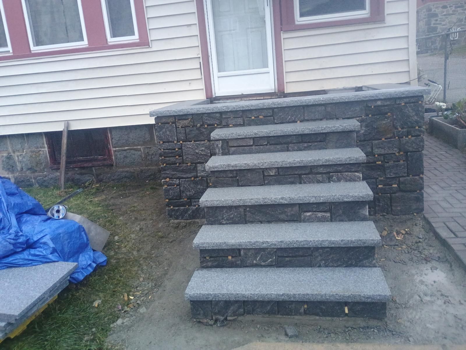 New stone entryway steps with granite treads leading up to the front door of a house with beige siding.