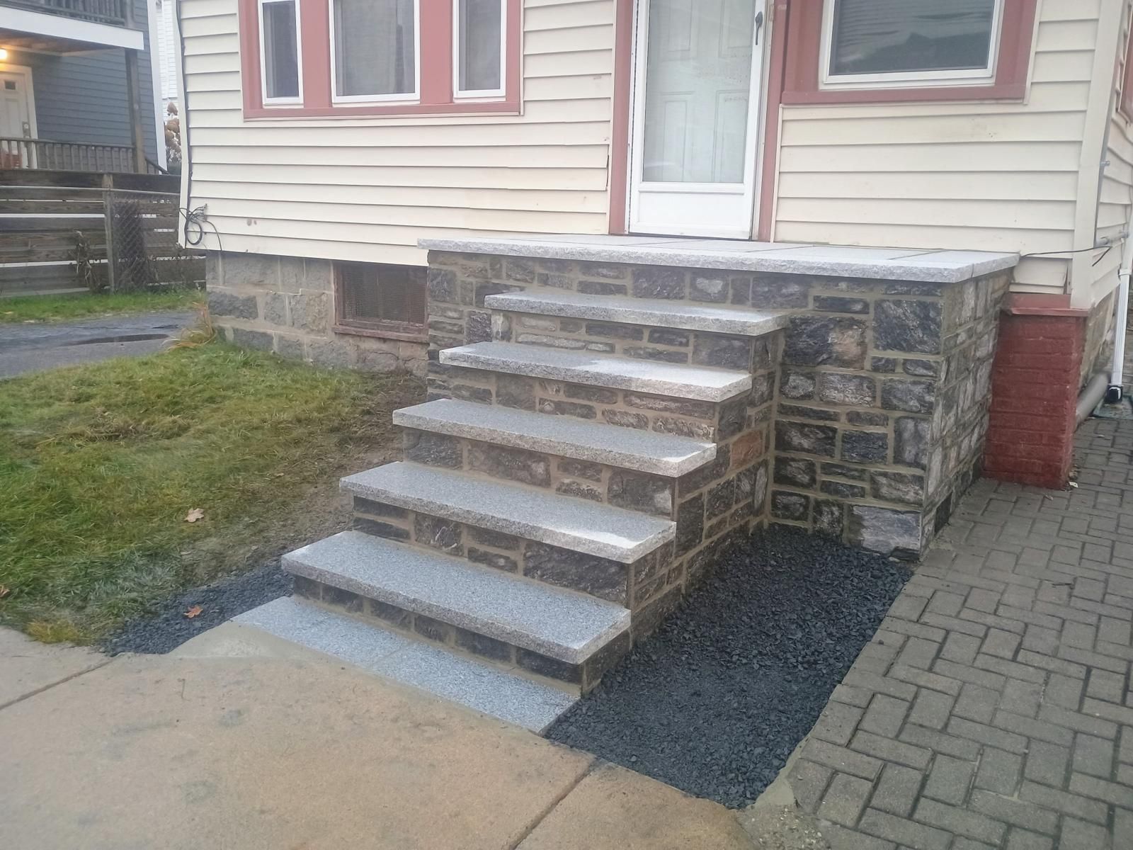 New stone front steps with gray granite treads leading to a house entrance next to a brick-paved walkway.