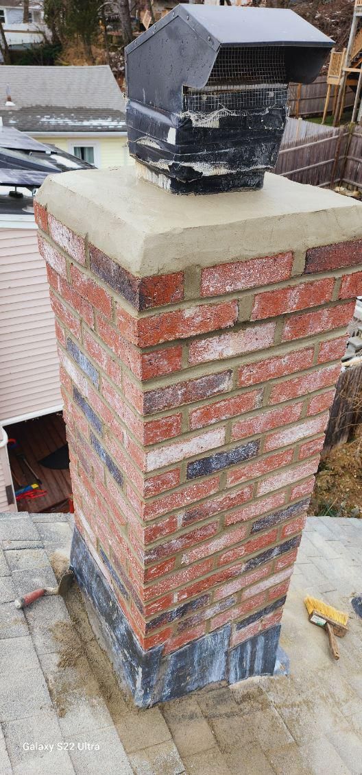 A freshly repaired brick chimney with a new concrete crown and black metal cap on a residential rooftop.