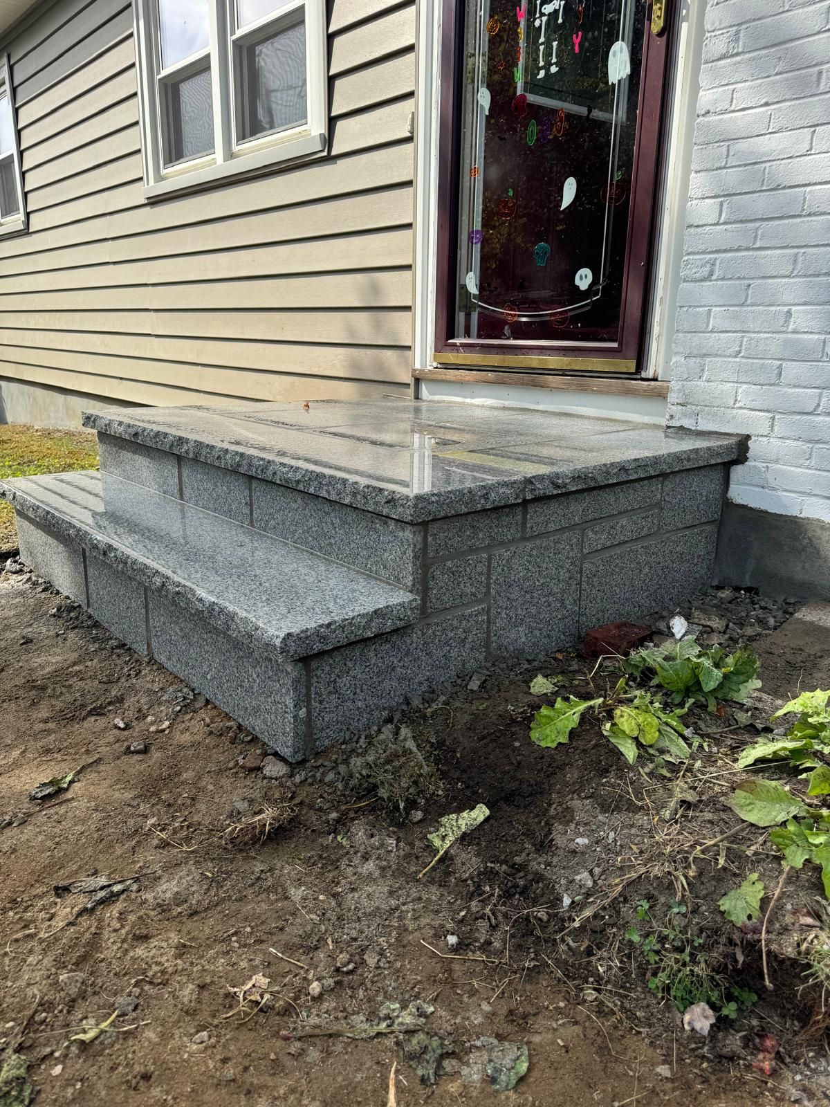 A newly installed gray, speckled stone step leading to a front door with tan siding and white painted brick exterior.