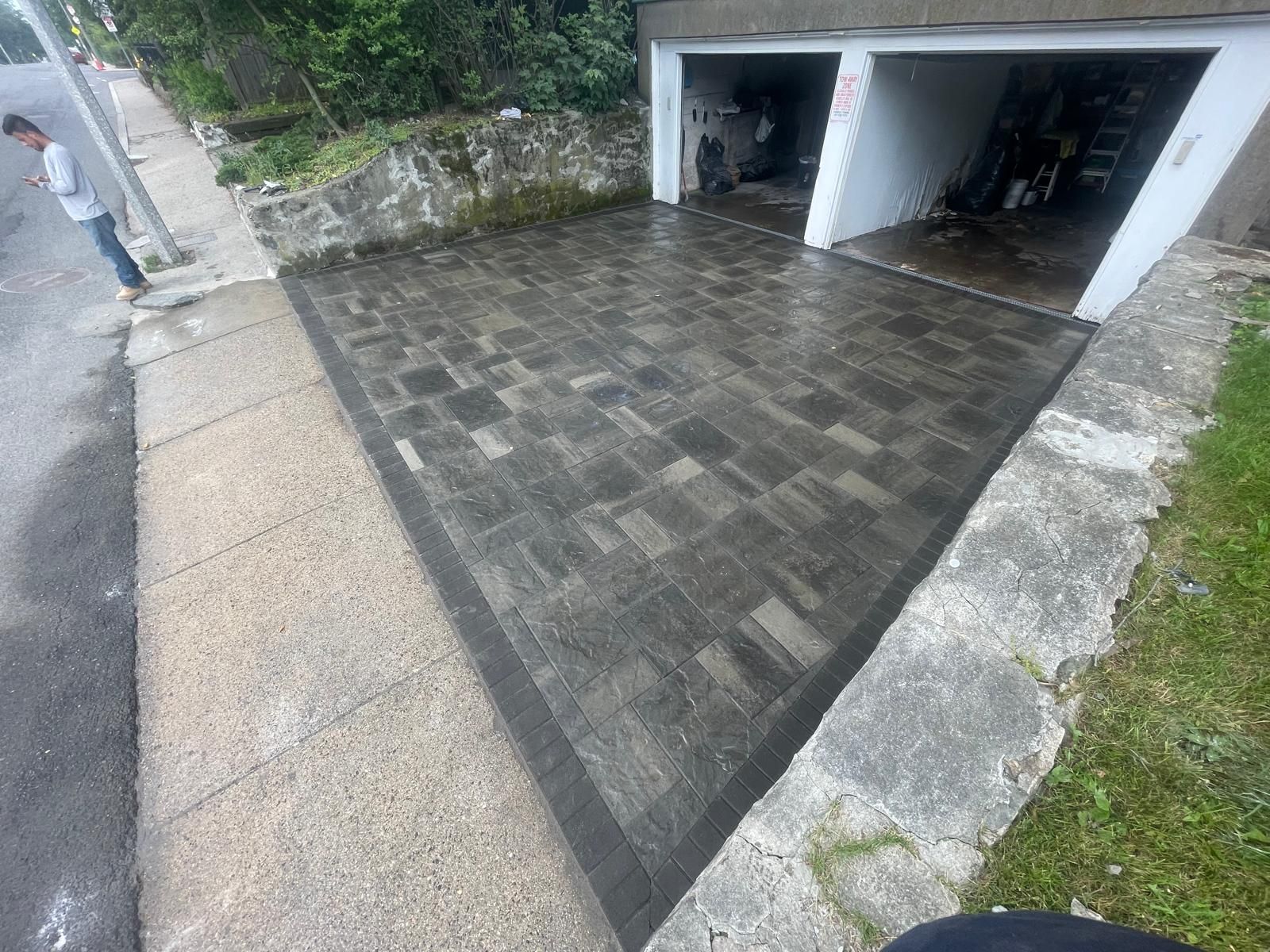 Newly installed gray paver driveway in front of a two-car garage, bordered by a dark concrete frame.