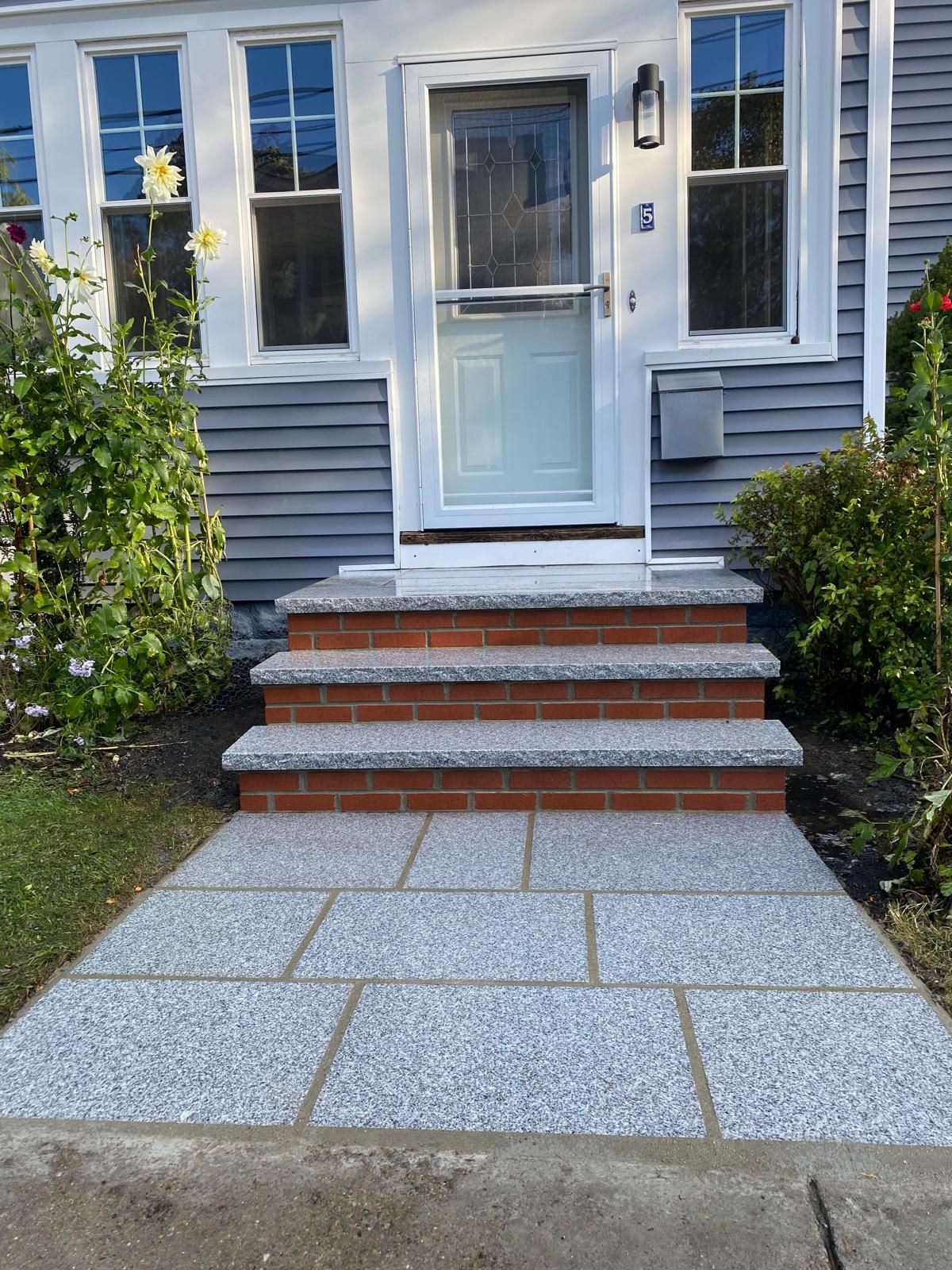 A house entrance with a grey stone walkway leading to three brick steps with speckled grey granite treads.