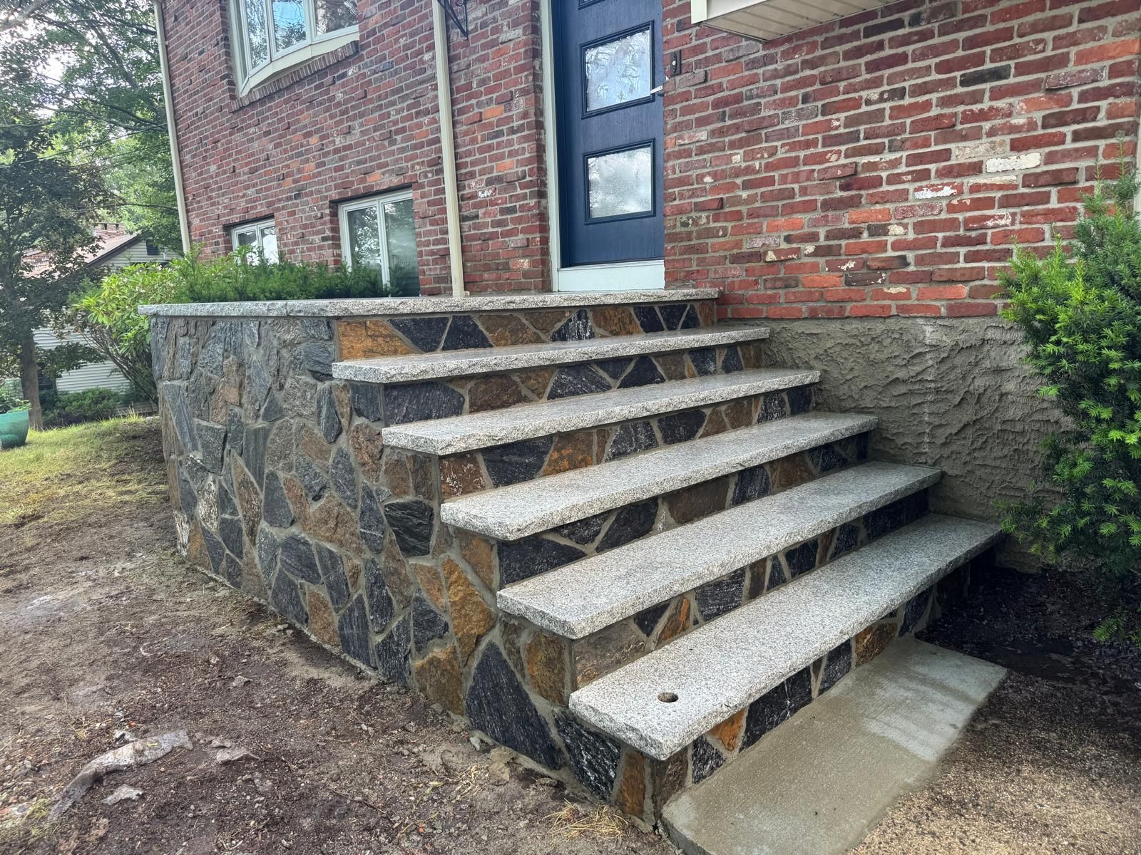 A set of granite steps with light stone treads and a dark, multi-colored fieldstone side wall leading to a front door.