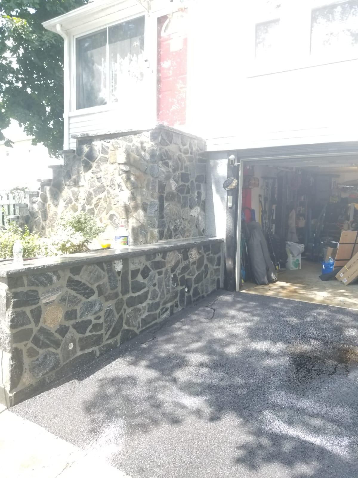 A house exterior featuring a stone retaining wall alongside a paved driveway leading into an open garage.