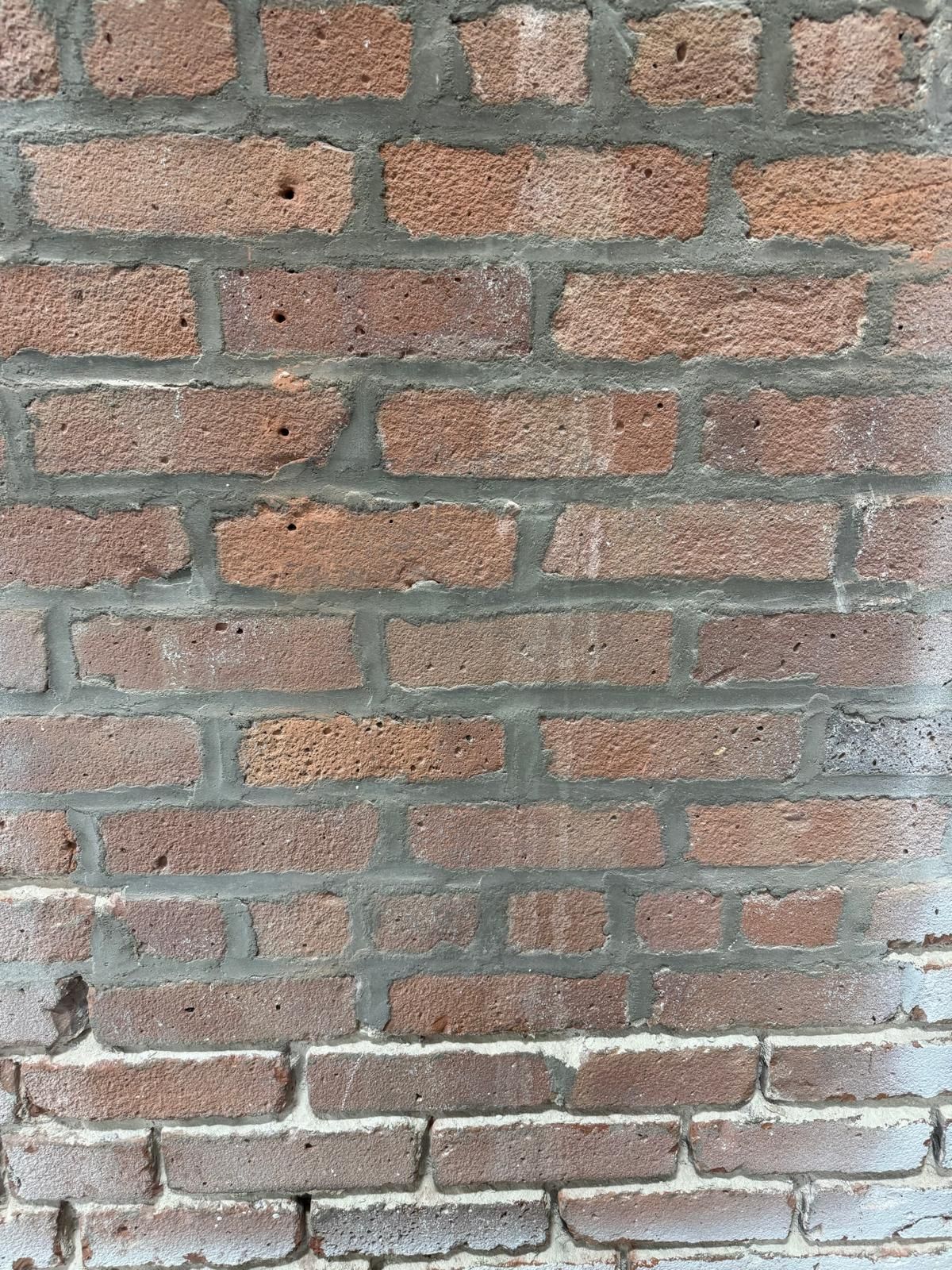A weathered, red brick wall with gray mortar joints, showing a subtle transition in brick texture toward the bottom.