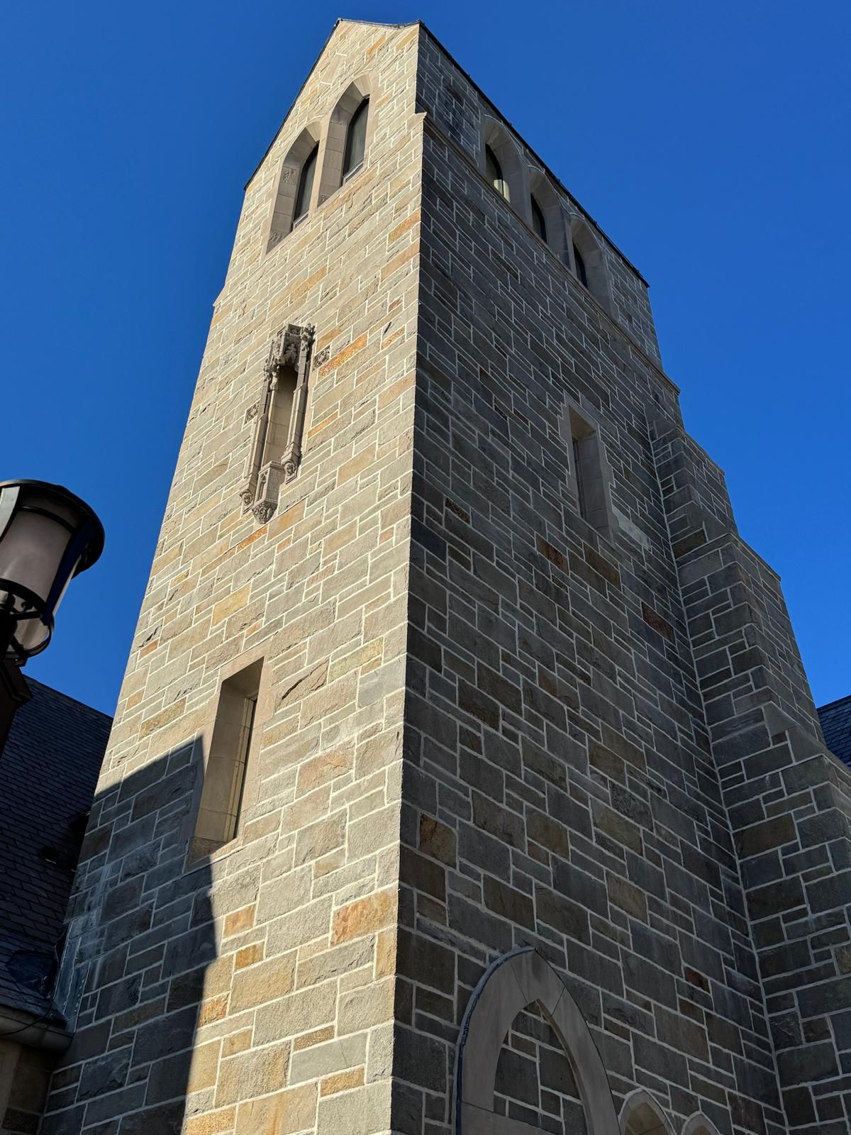A tall, narrow stone bell tower of an old church against a bright blue sky.