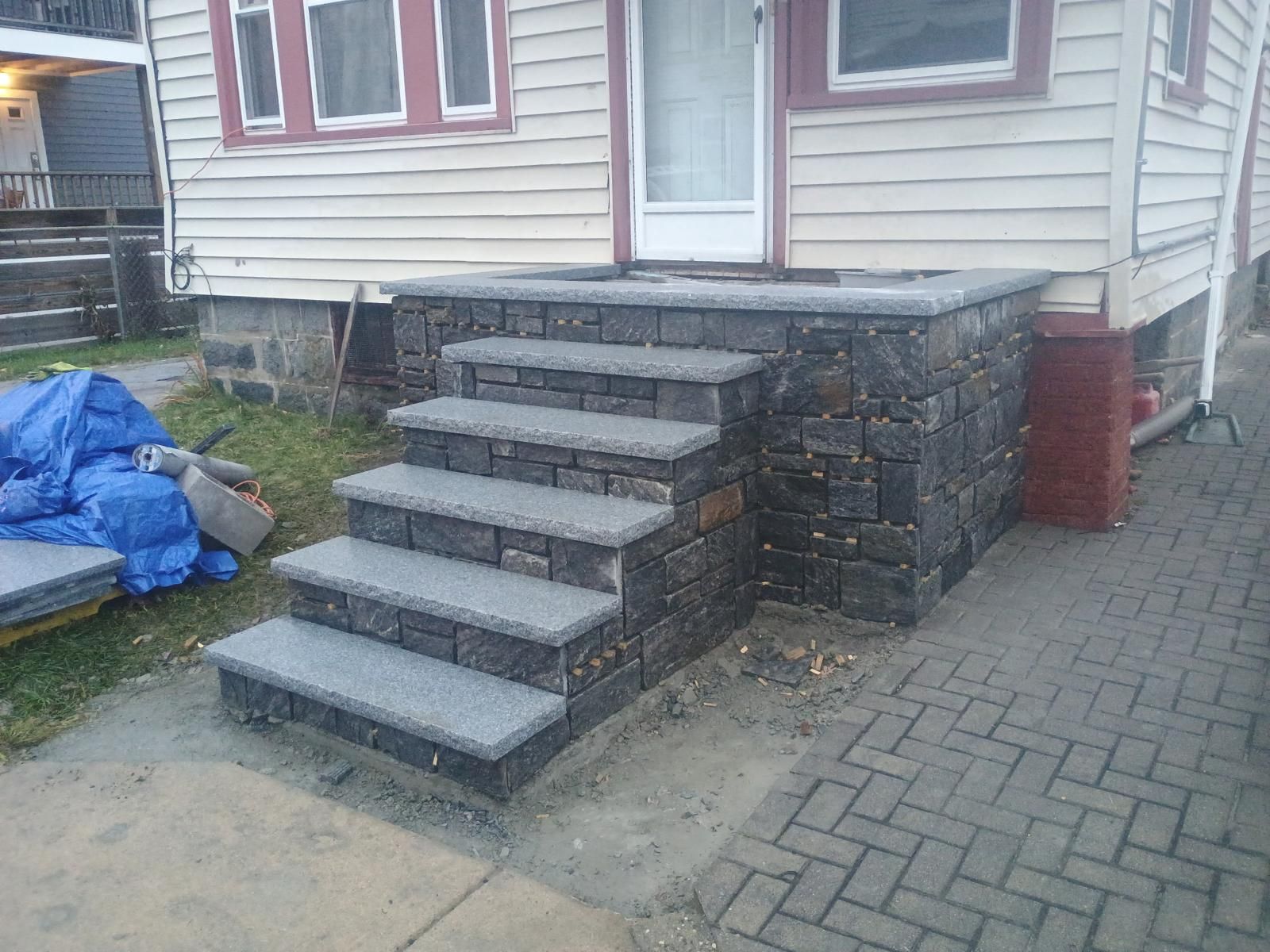 A set of new grey stone steps leading up to the white-sided house entrance, next to a paved driveway.