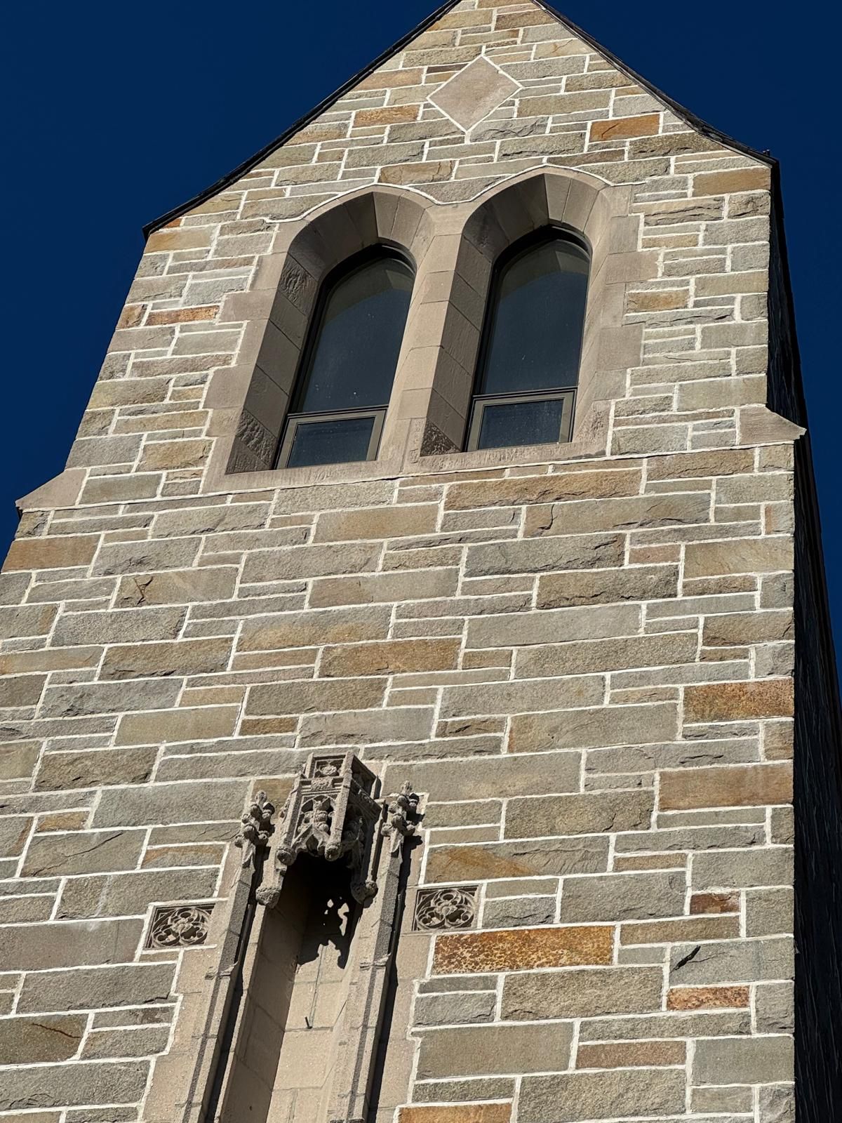 A stone church tower with two arched windows and a central decorative alcove against a clear blue sky.