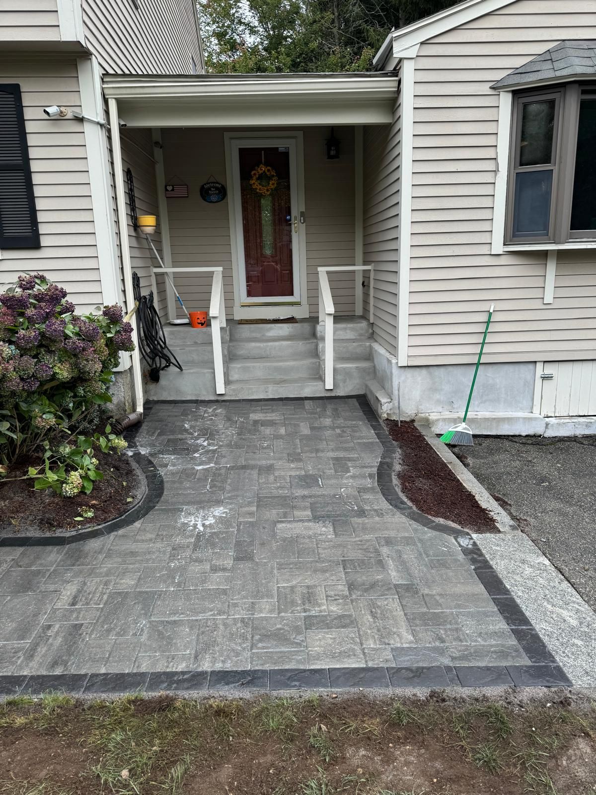A newly installed grey paver walkway leading to a house entrance with steps and white railings.