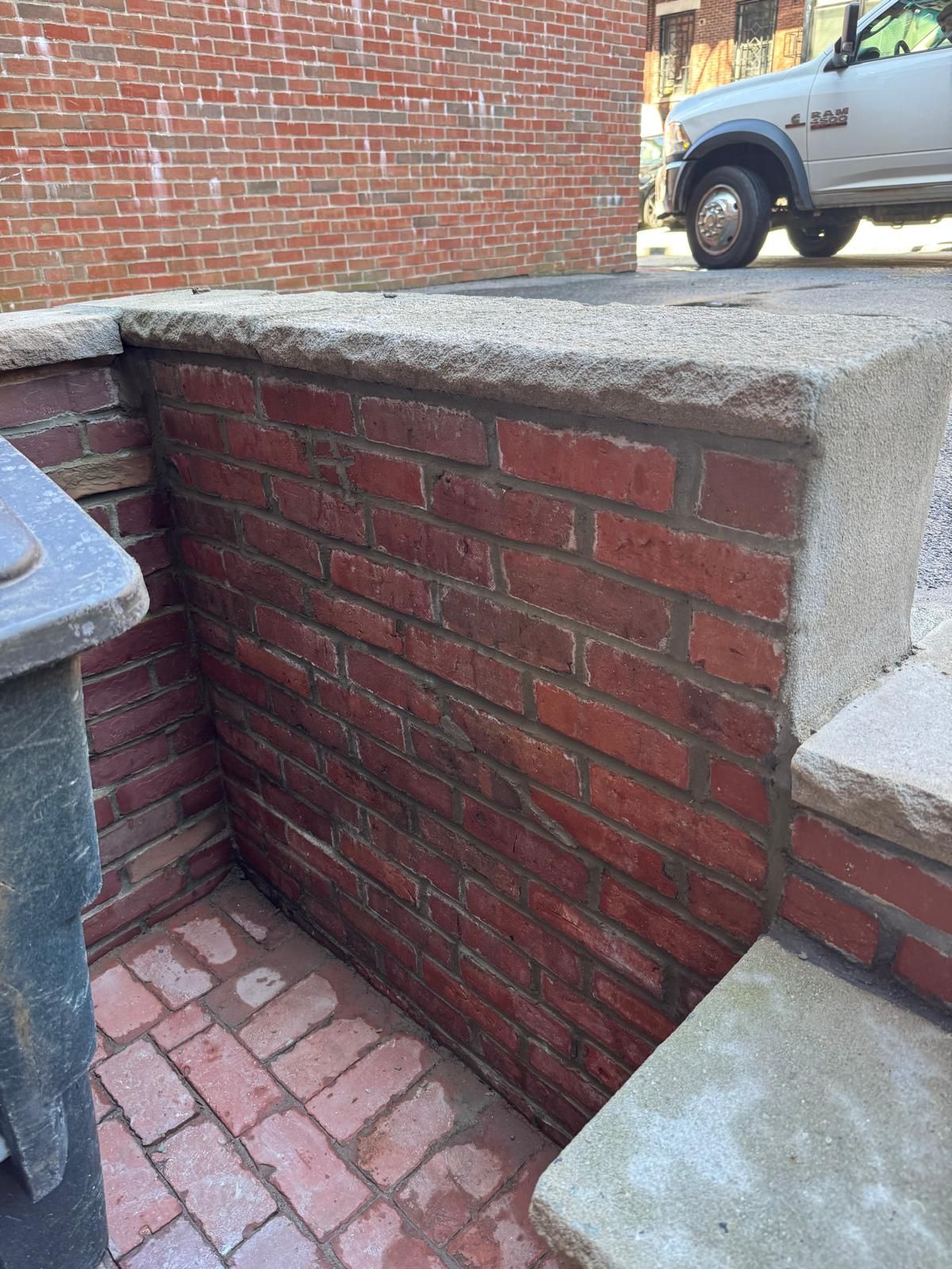 A brick retaining wall with a concrete cap, next to a brick-paved ground area, with a truck parked in the background.