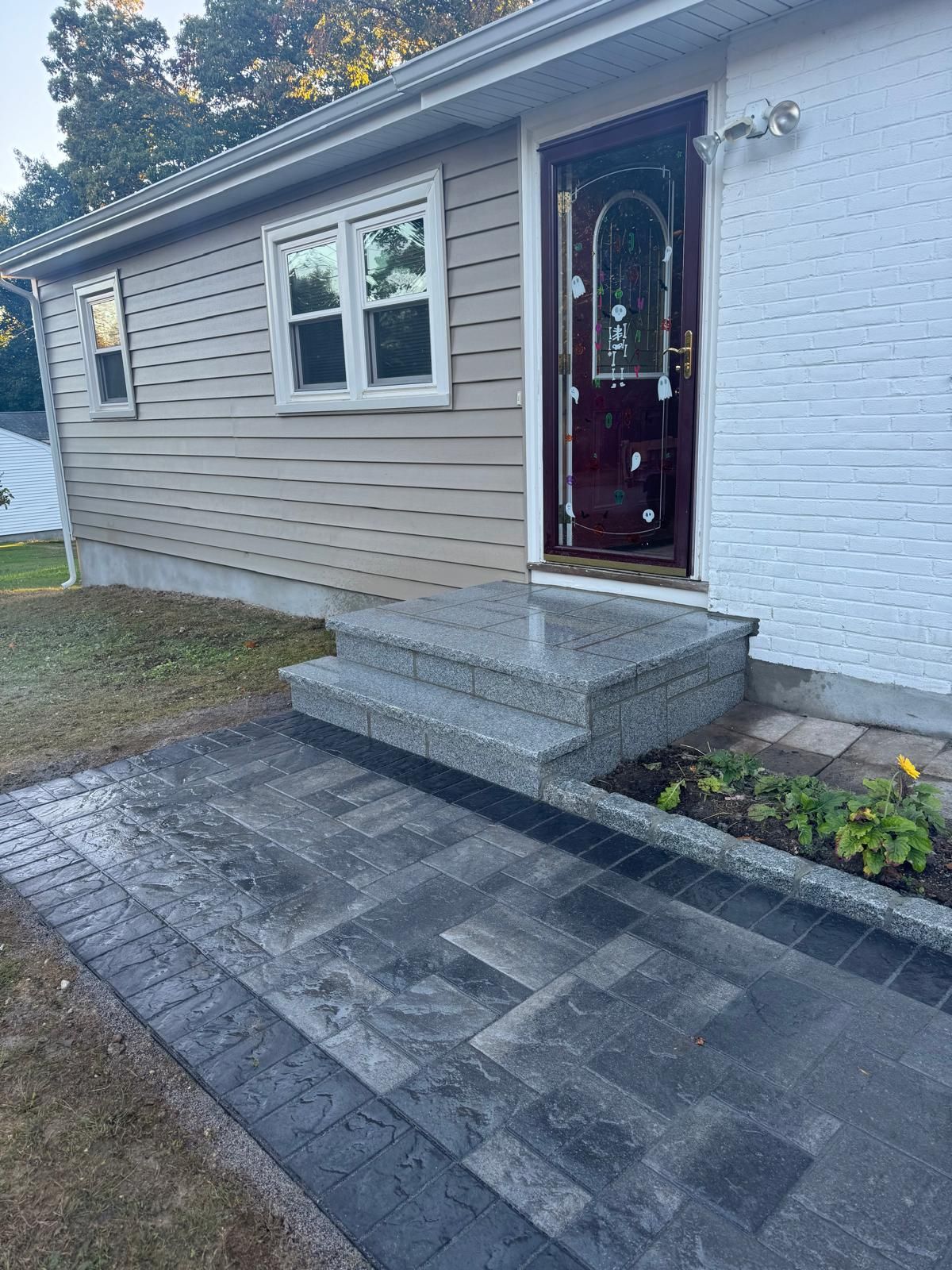 New stone steps and a paved walkway lead to the front entrance of a house with beige siding and white brick.