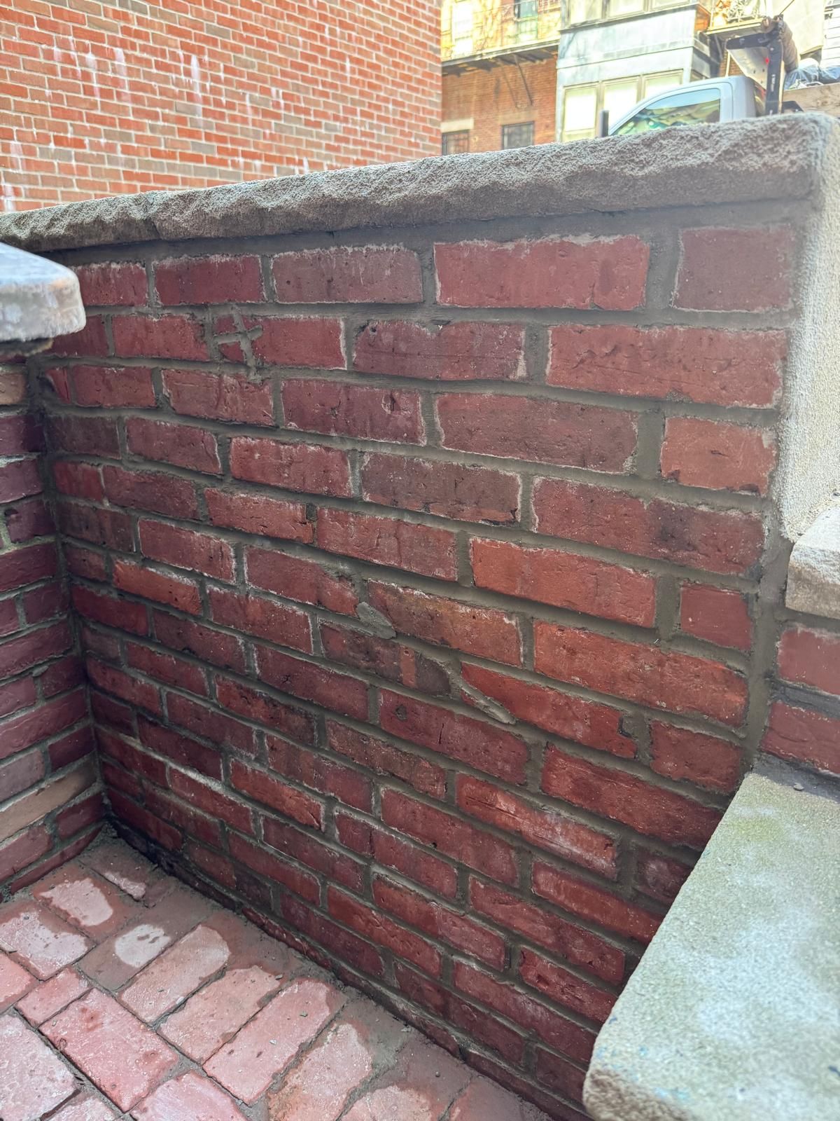 A red brick wall with gray mortar joins a stone cap and a brick patio in an outdoor corner.