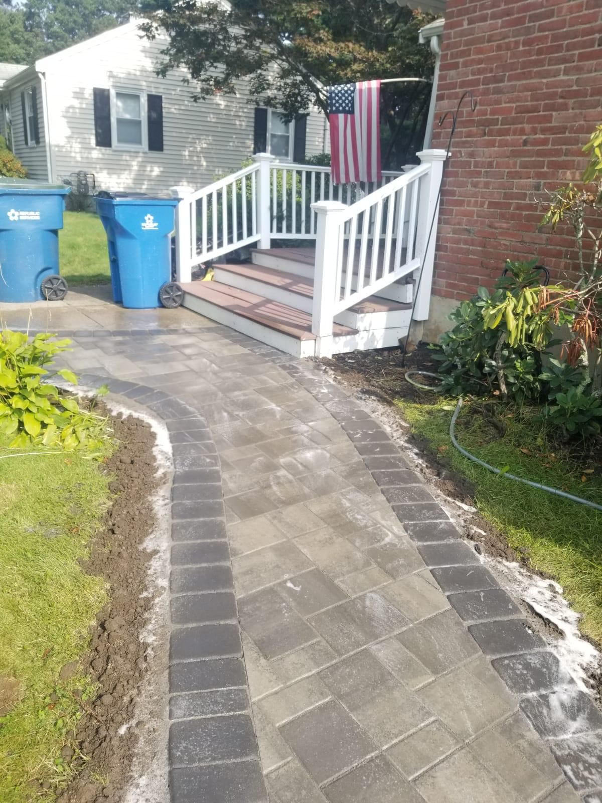 A newly installed stone paver walkway leading to white front porch stairs and a red brick house with an American flag.