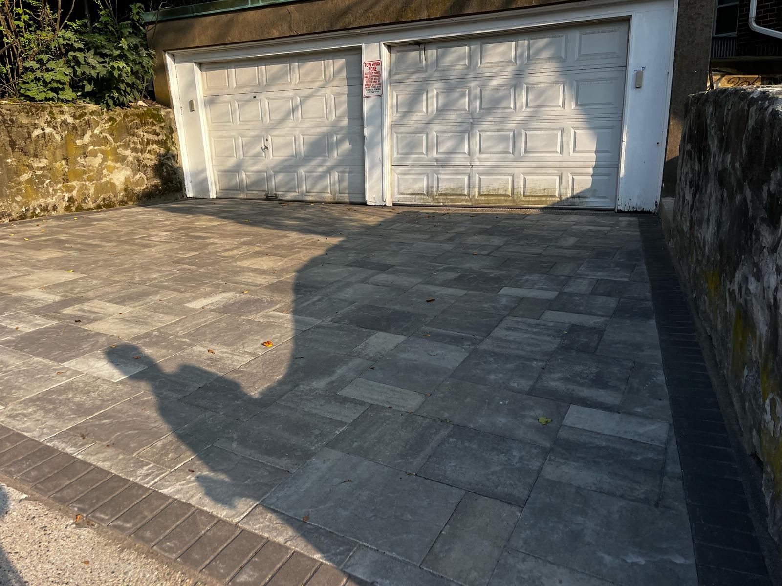 A newly paved driveway made of gray interlocking stone squares with a dark border, leading to a two-car garage.