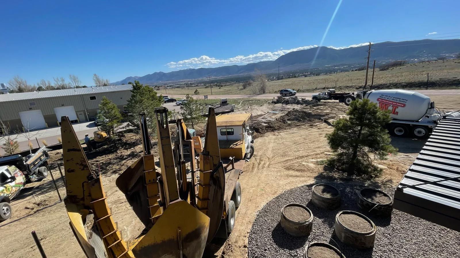 A concrete mixer truck is driving down a dirt road next to a row of construction vehicles.