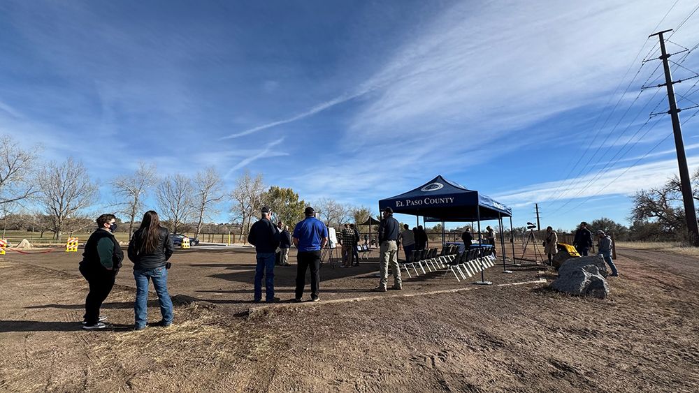 A group of people are standing in a dirt field in front of a blue tent.