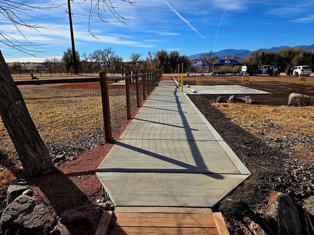 A concrete walkway going through a field with a wooden fence.