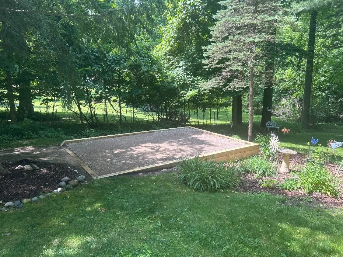 A sandbox is sitting in the middle of a lush green yard surrounded by trees.