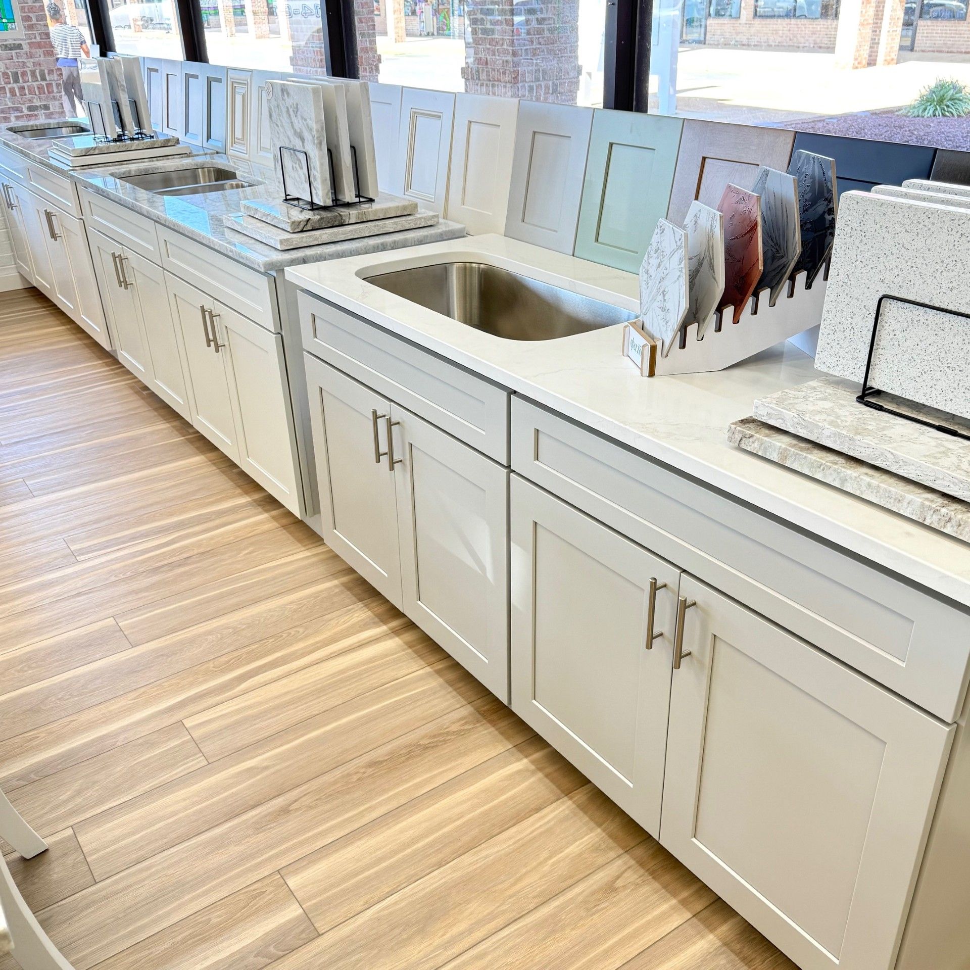 White kitchen cabinets with sample countertops and sinks displayed in a showroom.