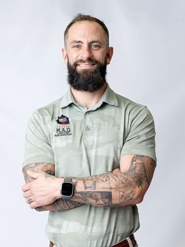 Man with beard and tattooed arms standing with arms crossed in a light green polo shirt