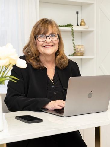 Woman smiling at a desk with a laptop in a bright white home office