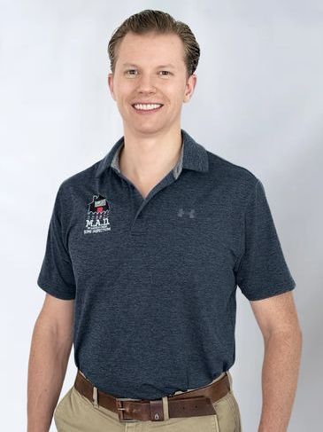 Smiling man in a navy polo and khaki pants standing against a light gray background
