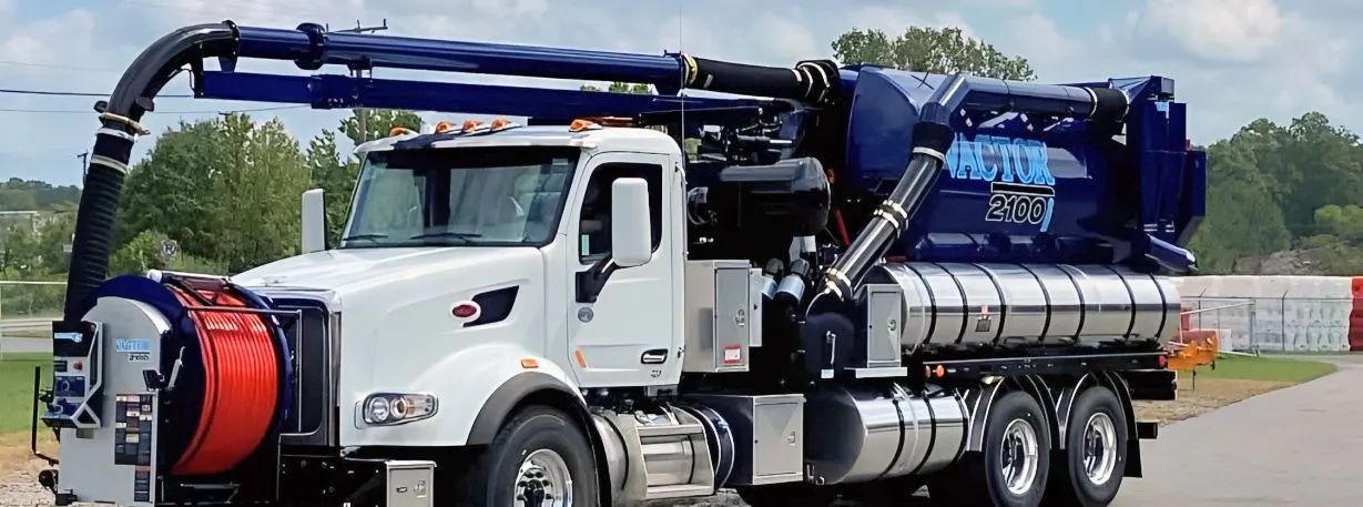 White vacuum truck with blue tank and hose equipment parked outdoors on pavement.