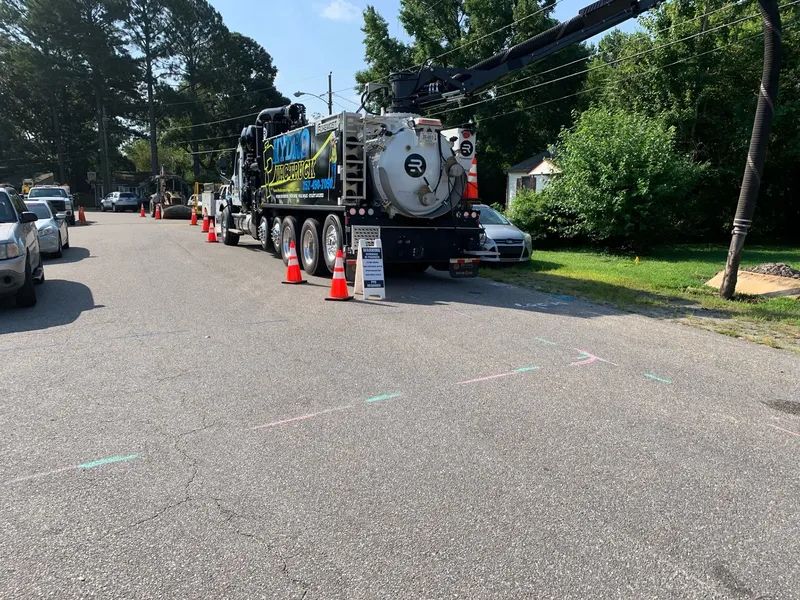 Utility truck and workers with orange cones on a residential street, clearing a roadside area.