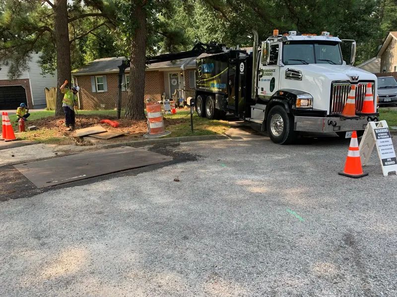 Utility truck at a roadside work zone with cones, a closed street, and a house in the background