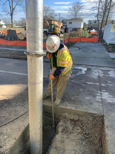 Construction worker digging around a utility pole on a sidewalk near a road repair site