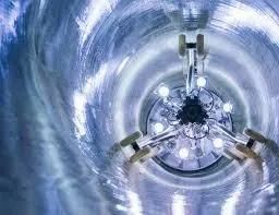 Inside a circular tunnel, a metallic structure glows with bright lights against blue swirling walls