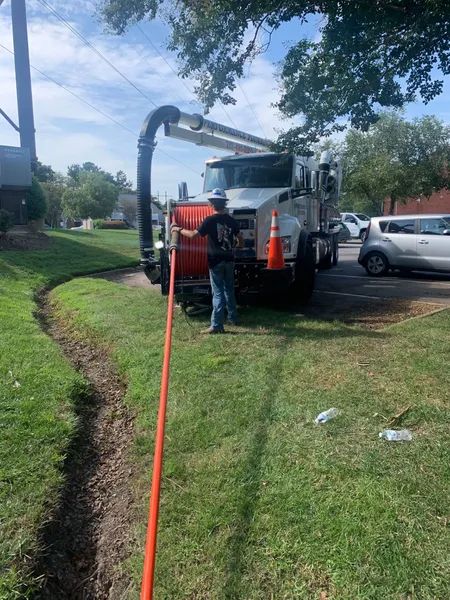 Utility truck parked on a grassy roadside with a worker and orange safety cones.