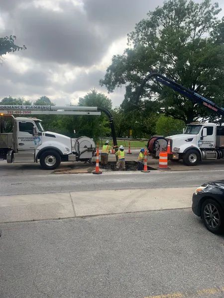 Utility workers and trucks repairing a road beneath overcast skies, with traffic cones marking the area