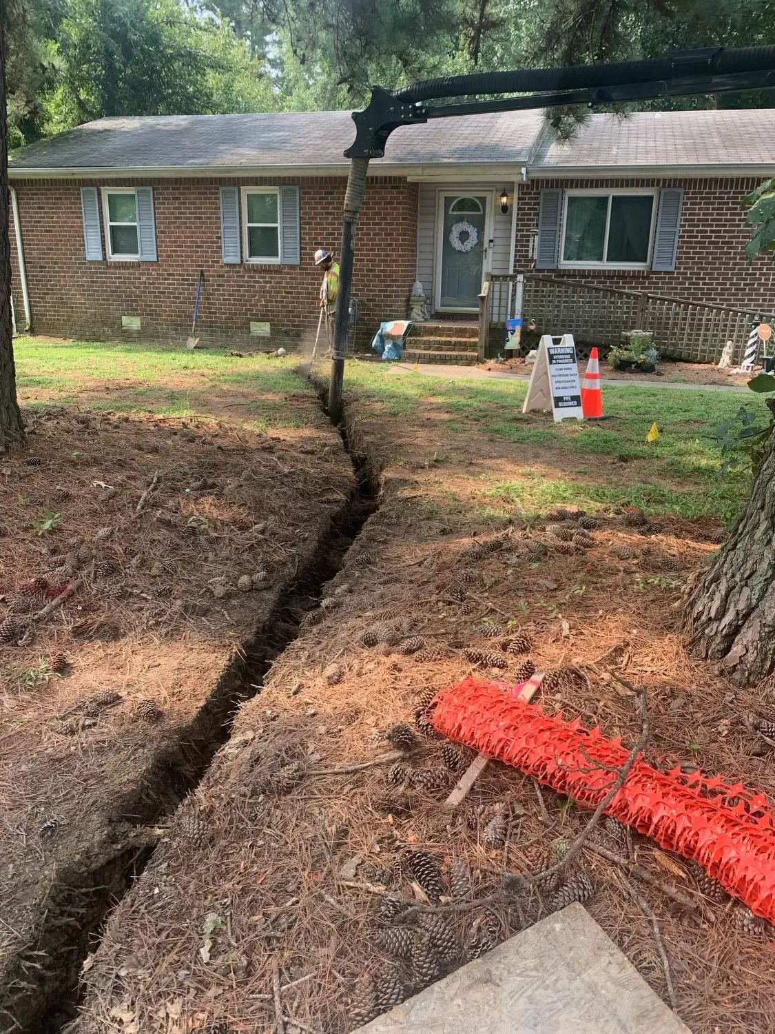 Large crack splitting a yard in front of a brick house, with orange safety cones nearby.