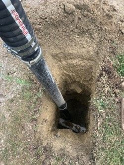 Black pipe or pole inserted into a deep hole in bare ground next to a grassy edge.