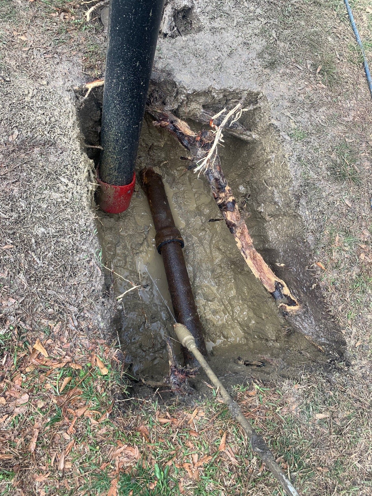 Exposed broken pipe in a muddy ground trench beside a black utility post