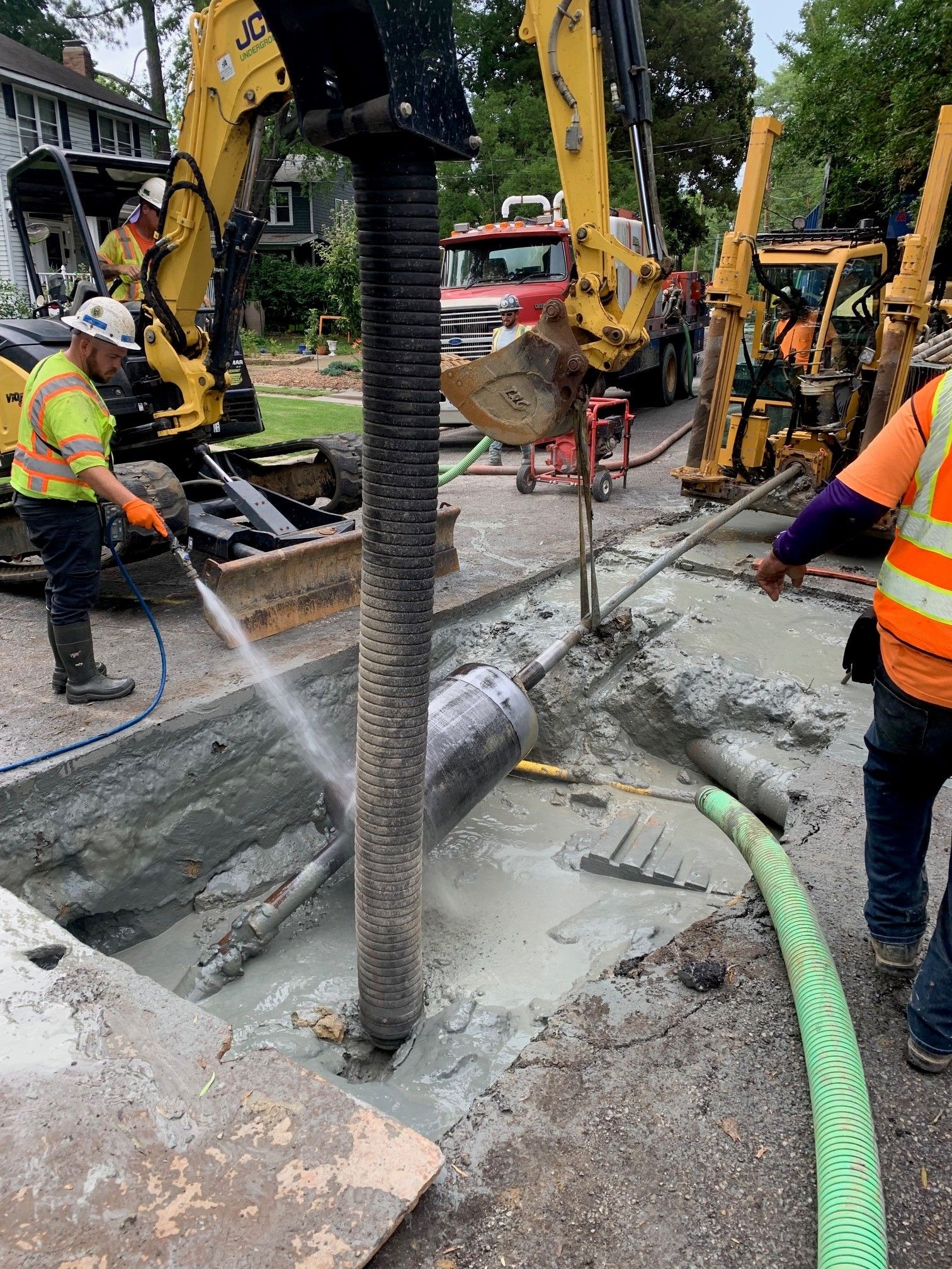 Construction workers repairing a road around a bent utility pole, with excavators and wet concrete nearby