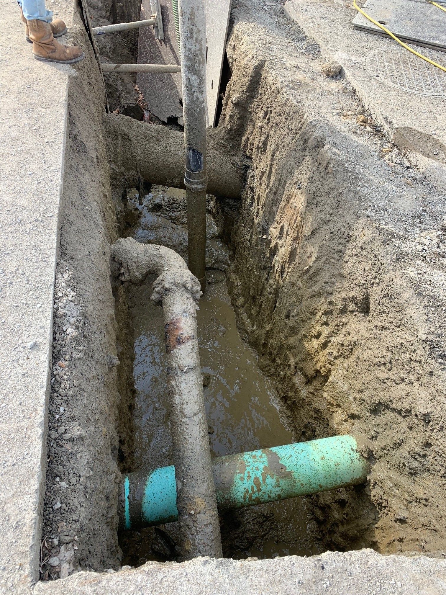 Trench with exposed pipes and muddy water between concrete walls at a construction site