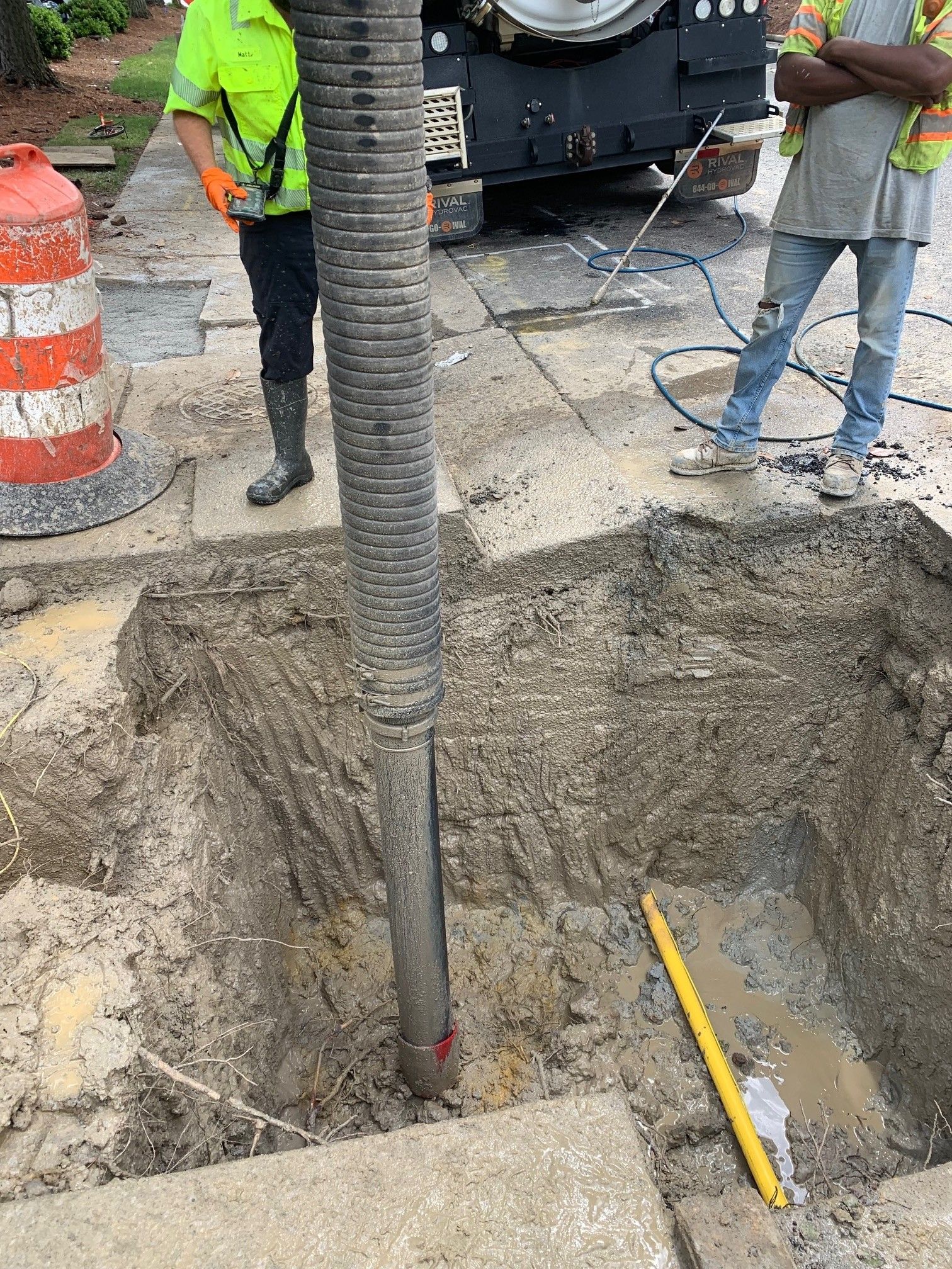 Roadwork crew at a street excavation with a large utility pole and tools in a dirt trench