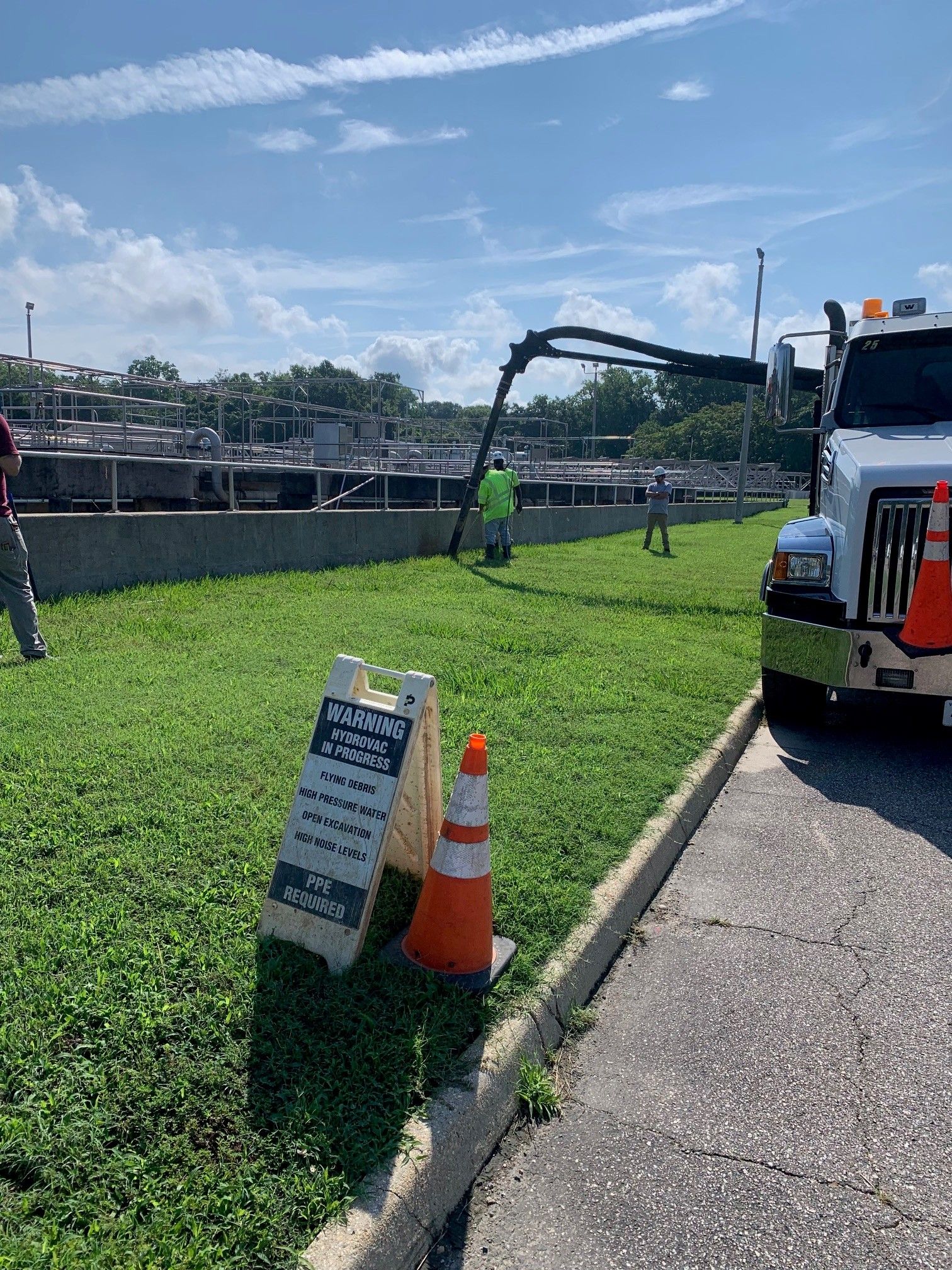 Construction worker beside roadside trench with orange cone and utility truck under blue sky