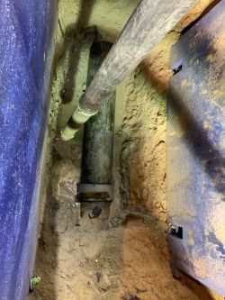 Narrow utility space with exposed pipes, dusty floor, and insulated walls in dim light