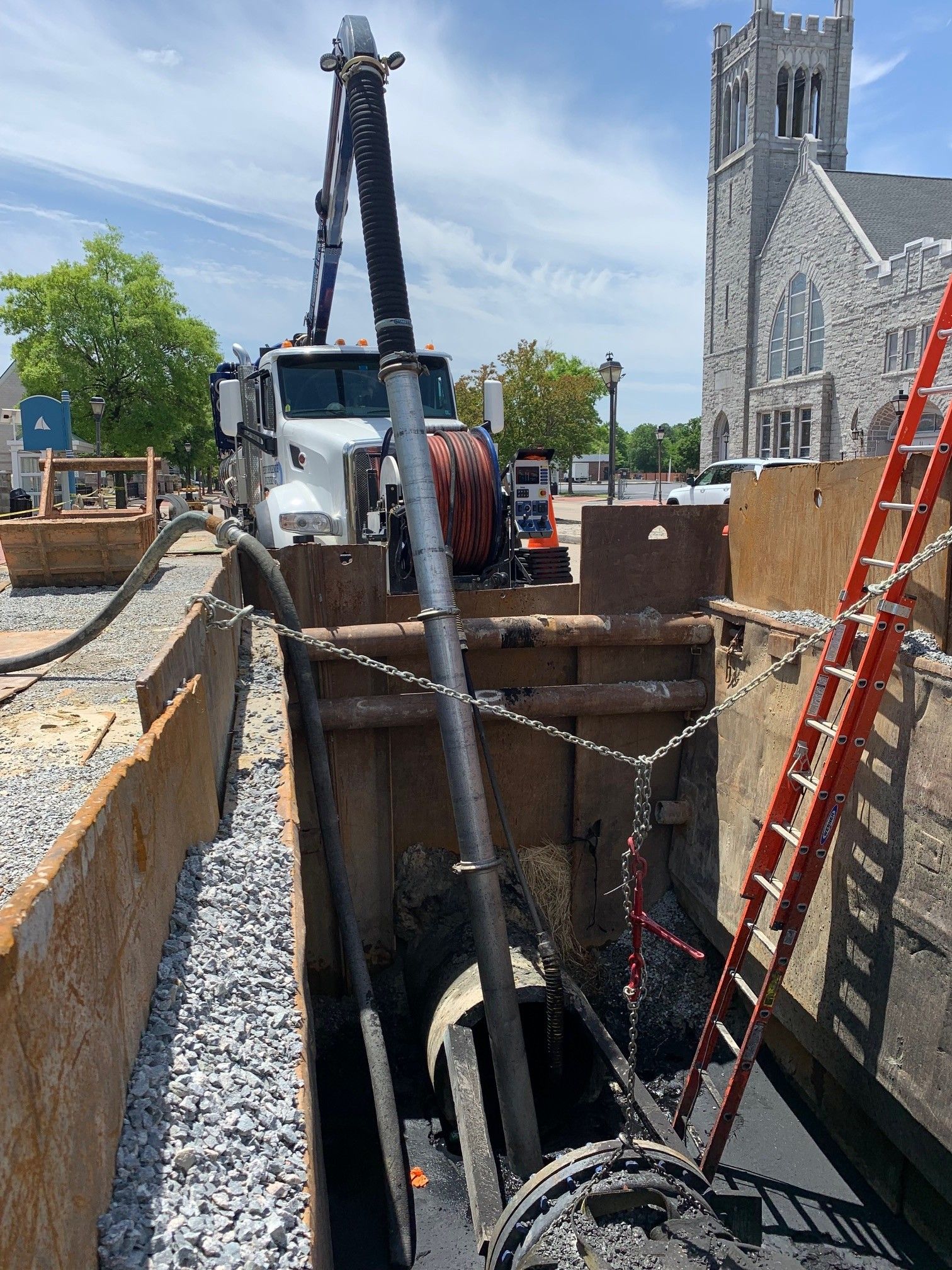 Construction site with a crane over a deep trench beside a stone church and ladders.