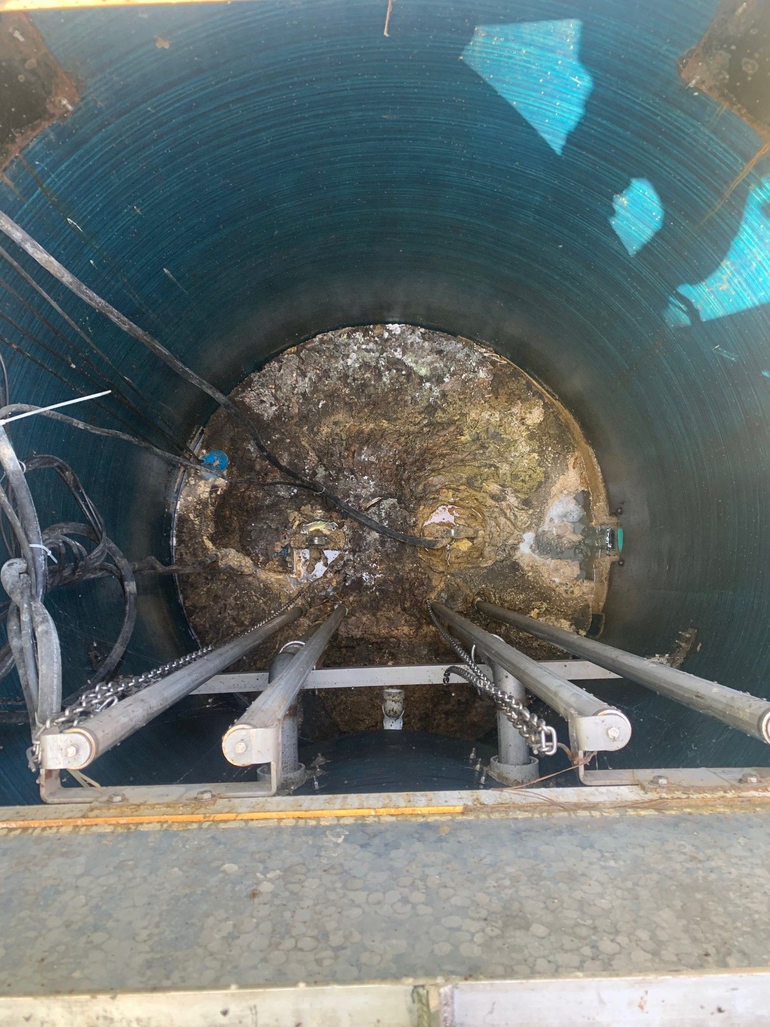 Inside a large blue pipe, three cables extend toward a debris-filled end blockage.
