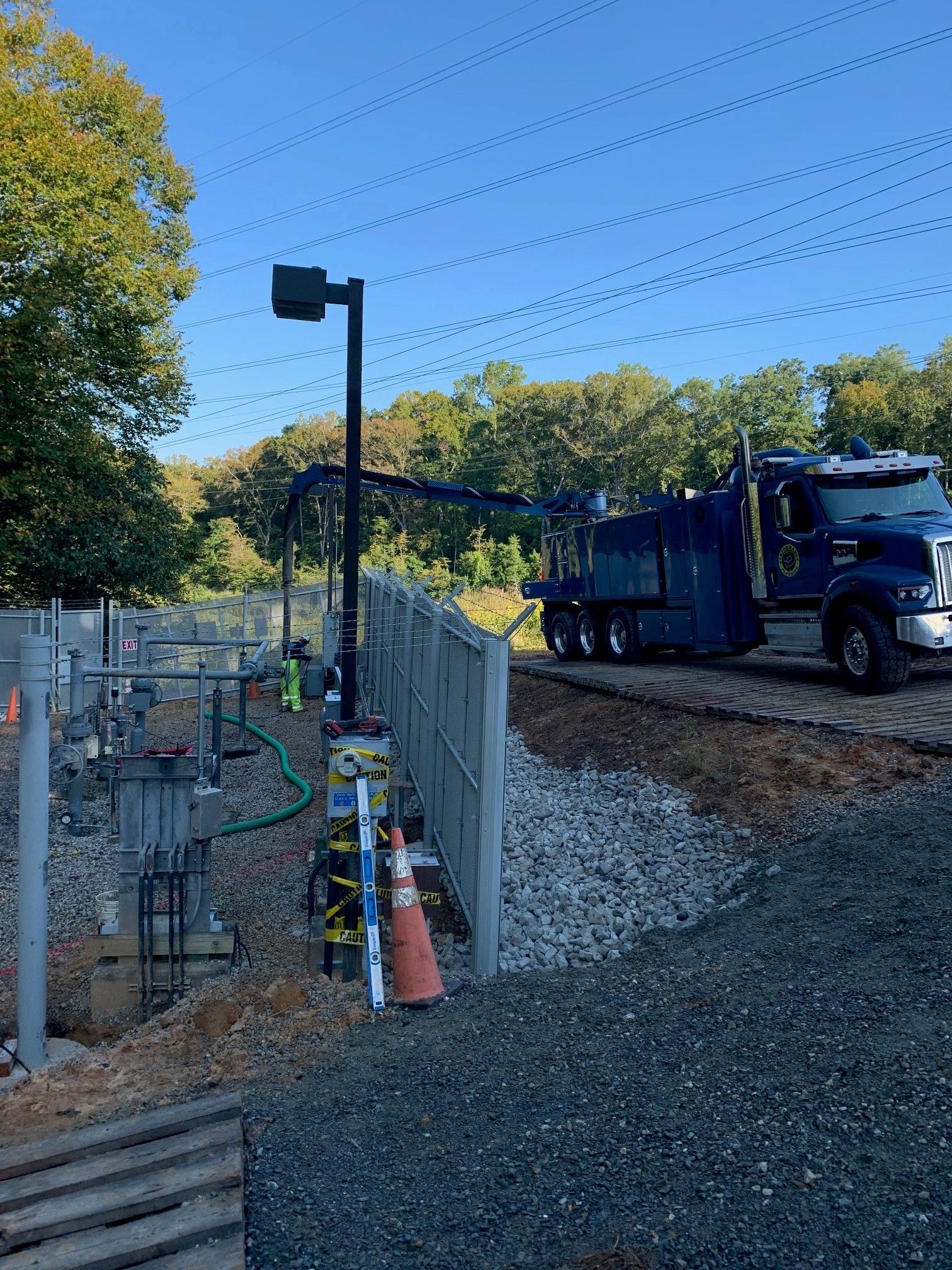 Blue truck and dump trailer beside a fenced gravel work area under a clear blue sky.