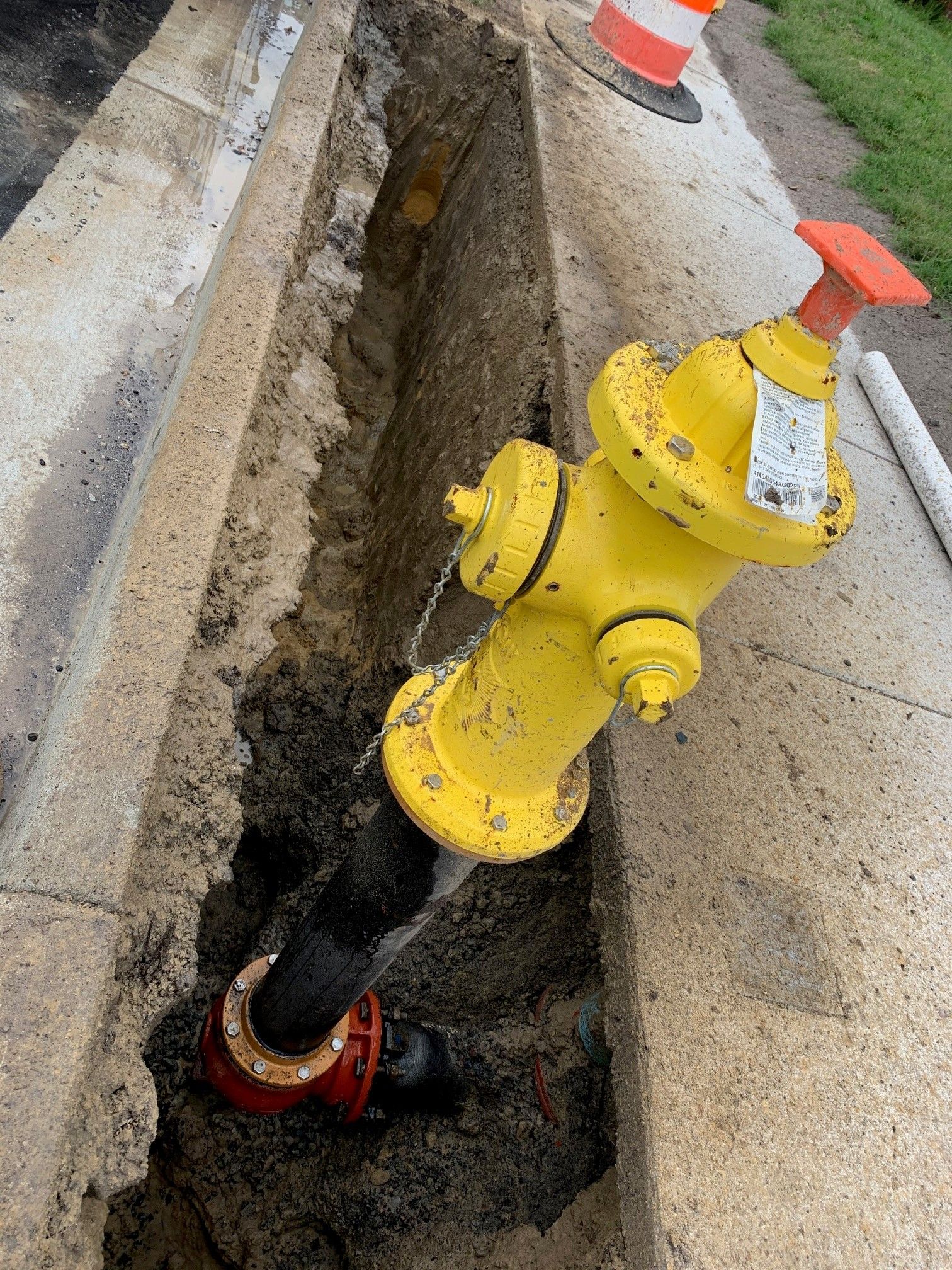 Yellow fire hydrant beside an open trench with exposed black pipe on a street corner