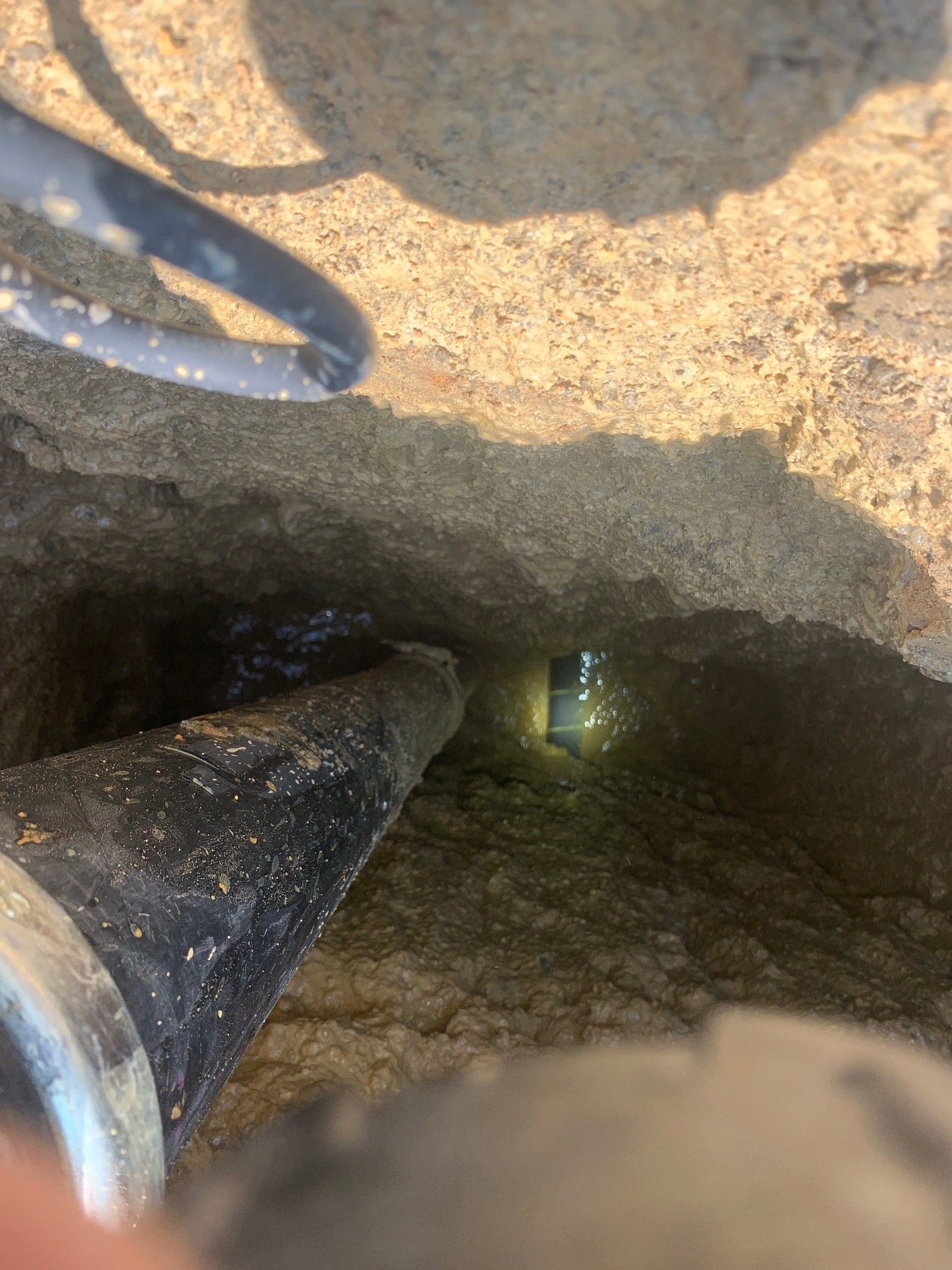 Inside a dirt hole, a black pipe points toward a small metallic fitting glinting in the darkness