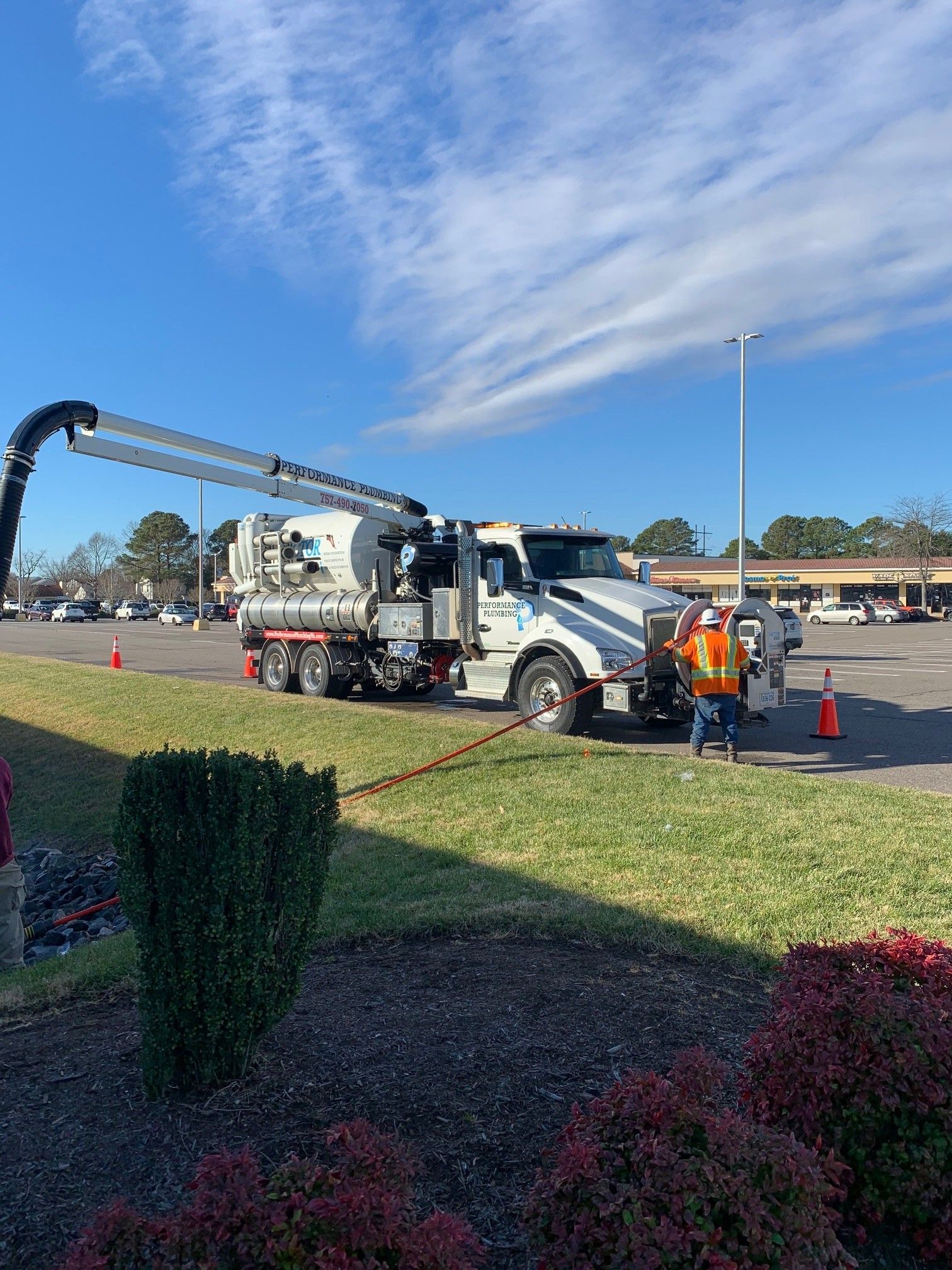 Utility truck with crane arm and workers on a roadside work site under a blue sky