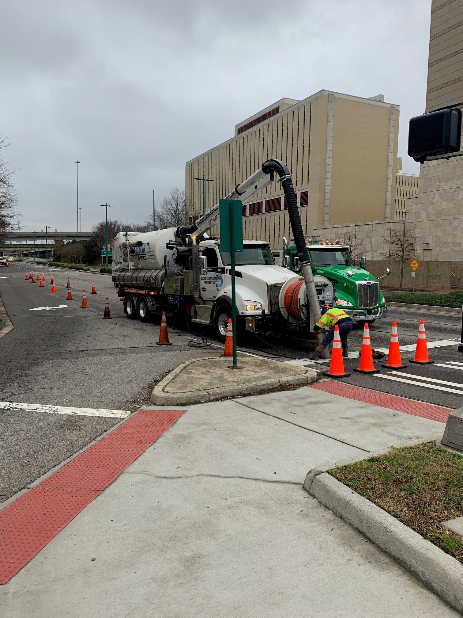 Utility truck and crew repairing roadside equipment beside a sidewalk, with orange cones and traffic barrels.