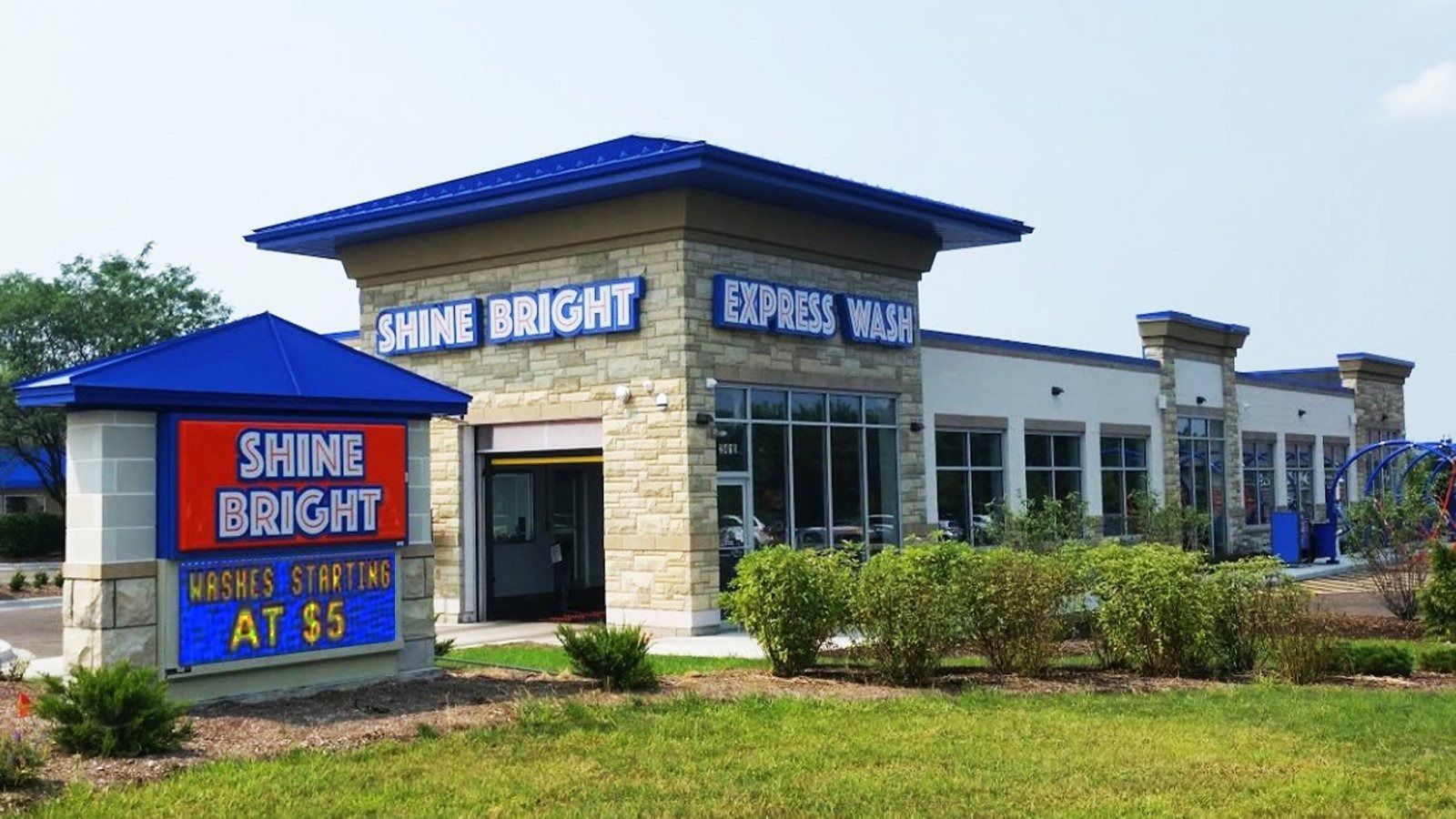 Shine Bright car wash building with blue roof and a roadside sign on a grassy lot