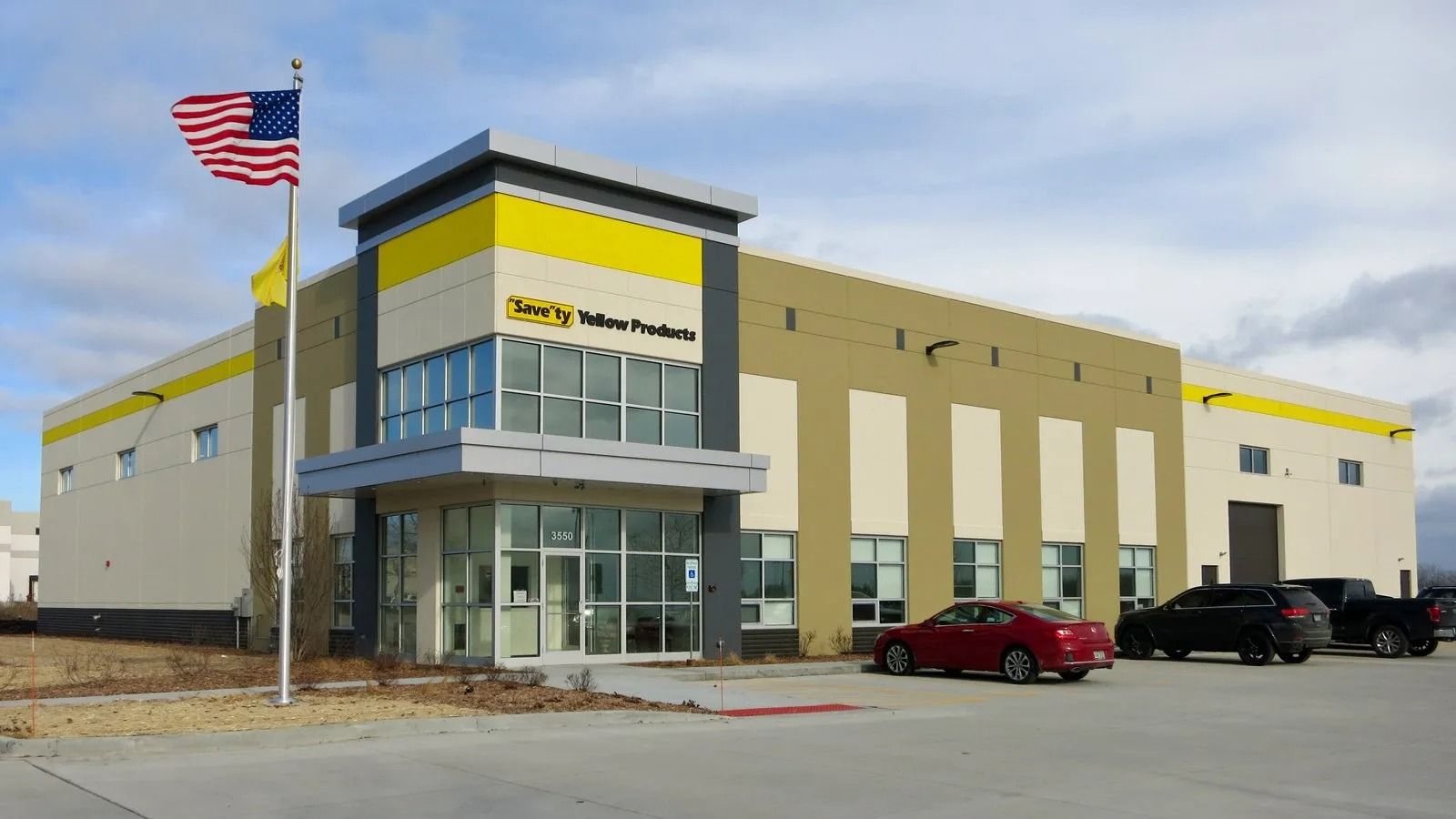 Modern warehouse storefront with glass entrance, American flag, and parked red and black cars